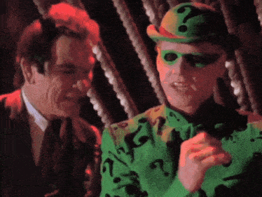 a man in a green hat with a question mark on it is talking to another man