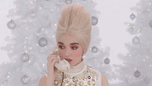a woman in a wig is talking on a phone in front of a white christmas tree