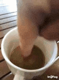 a person 's hand is reaching into a cup of coffee on a table .