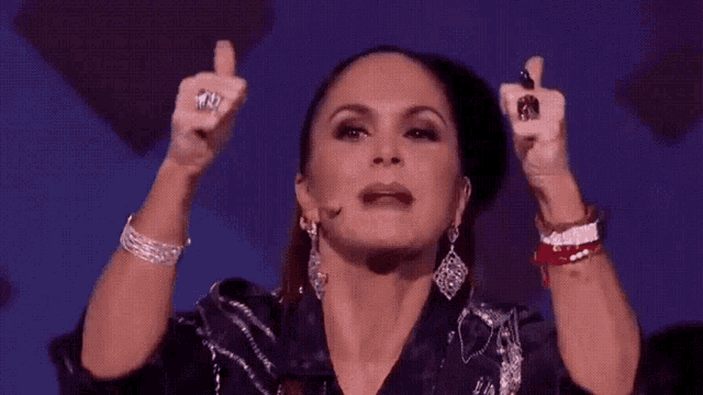 a woman wearing a black jacket and earrings is giving a thumbs up sign .