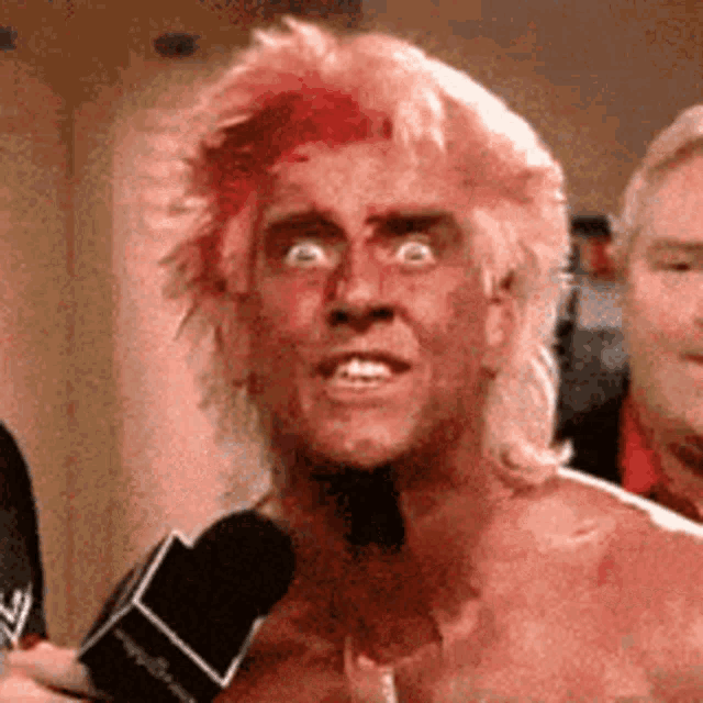 a man with red hair is talking into a microphone while another man looks on .
