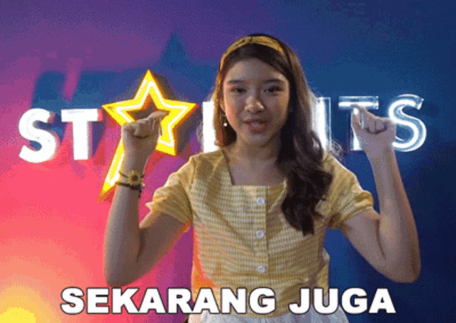 a girl in a yellow shirt is standing in front of a sign that says star hits