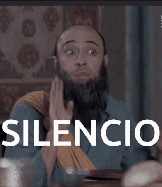 a man with a beard is sitting at a table and the word silencio is above him