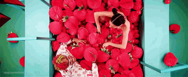 a man and a woman are laying in a box filled with red strawberries .