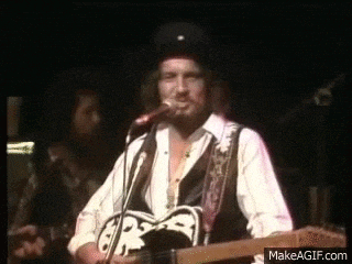 a man with a beard is playing a guitar and singing into a microphone on a stage .