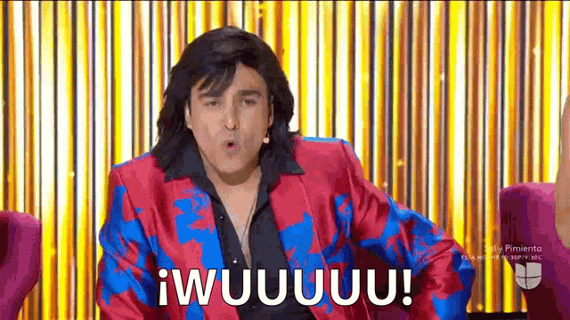 a man in a red and blue suit is sitting in a chair with his mouth open and says i wuuuu !