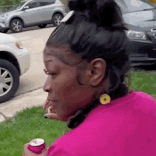 a woman in a pink shirt is sitting in the grass holding a can of soda .
