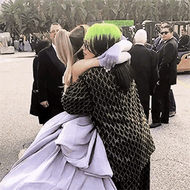 a woman with green hair is hugging another woman in a white dress .