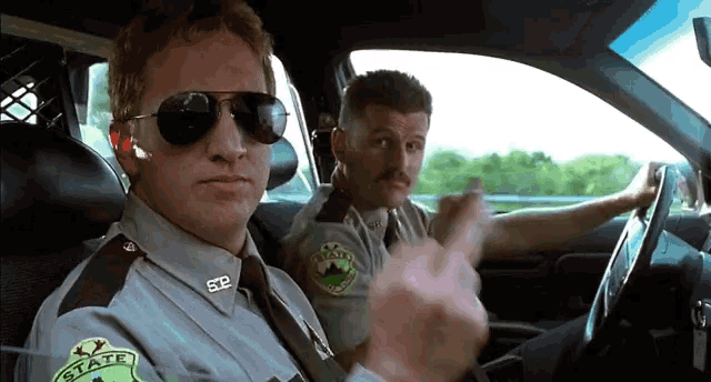 two sheriff 's officers are sitting in a car and one of them is giving the middle finger .
