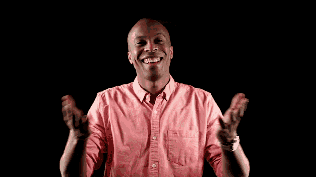 a man wearing a pink shirt is smiling with his arms outstretched