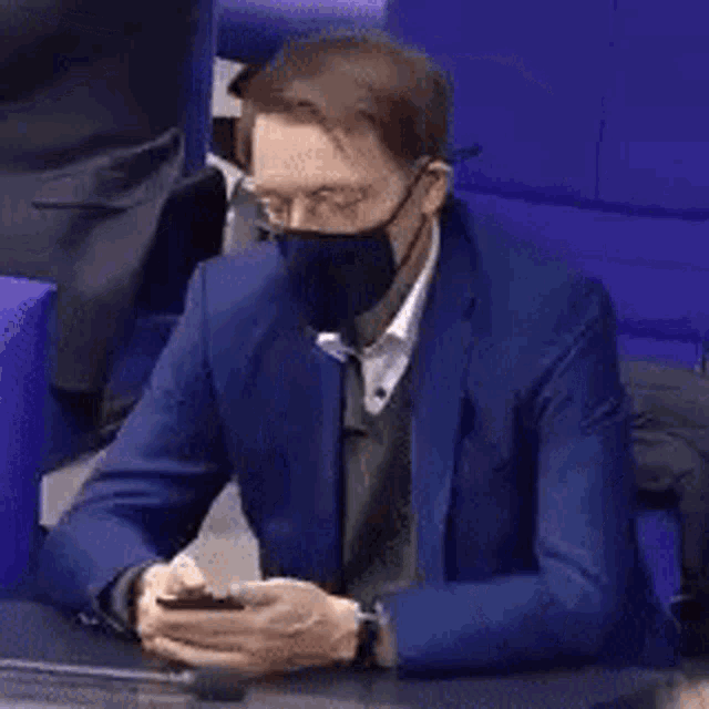 a man wearing a face mask and a blue suit is sitting in a chair .
