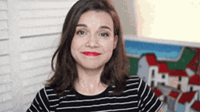 a woman in a black and white striped shirt is smiling in front of a window .