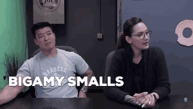 a man and a woman are sitting at a table and the man is wearing a shirt that says barbell on it