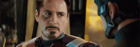 iron man and captain america are looking at each other in a room in a movie .