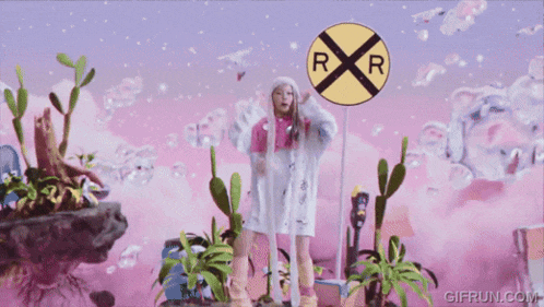 a woman wearing a pink jacket and a white hat is standing in front of a railroad crossing sign .