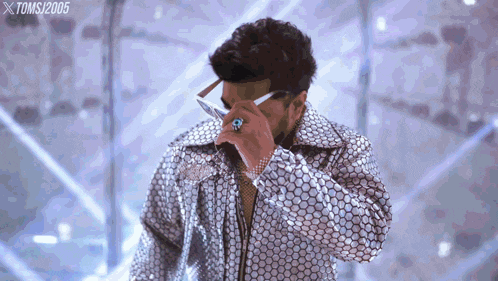 a man wearing a sequined jacket and sunglasses is standing in front of a sign that says xtoms 2005