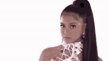 a woman with long dark hair in a ponytail is wearing a white top and earrings .