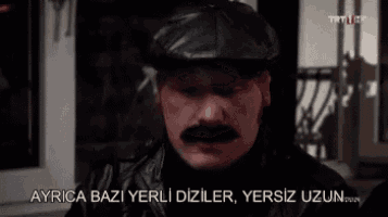 a man with a mustache and a hat is talking to another man in a foreign language .