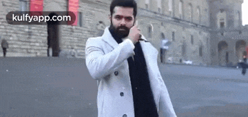 a man with a beard is talking on a cell phone while standing in front of a building .