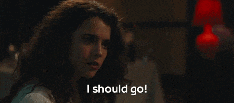 a woman with curly hair is standing in a dark room and says `` i should go '' .