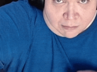 a woman in a blue shirt is making a funny face with her finger in her mouth .