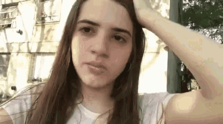 a young woman with long hair is holding her hand to her head and making a funny face .
