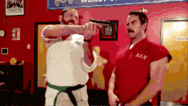 a man in a red ken uniform is pointing a gun at another man in a white shirt