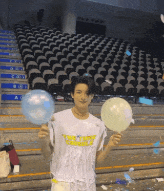 a young man holding two balloons in front of an empty auditorium