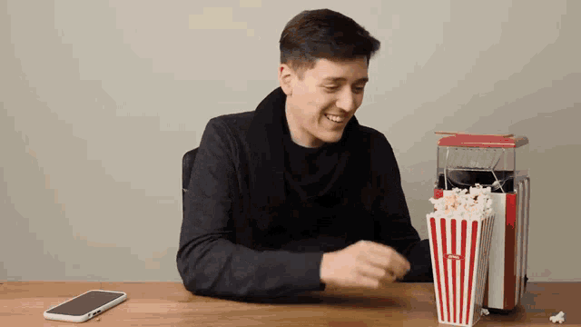 a man is sitting at a table with a popcorn maker and a phone