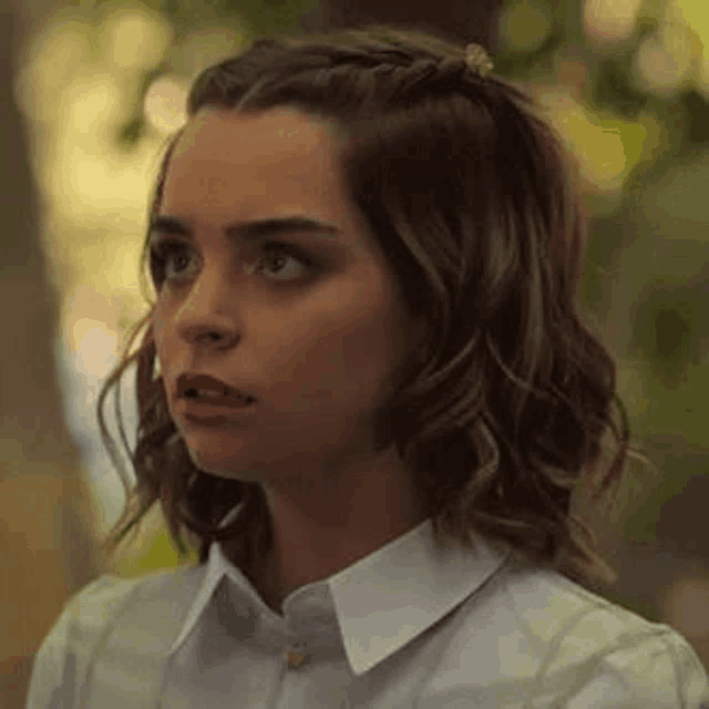 a close up of a woman 's face with a white shirt and a braid in her hair .