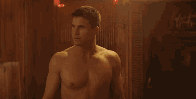 a shirtless man is standing in front of a wooden wall and says what
