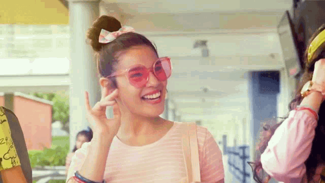 a girl wearing pink sunglasses is smiling and giving the peace sign