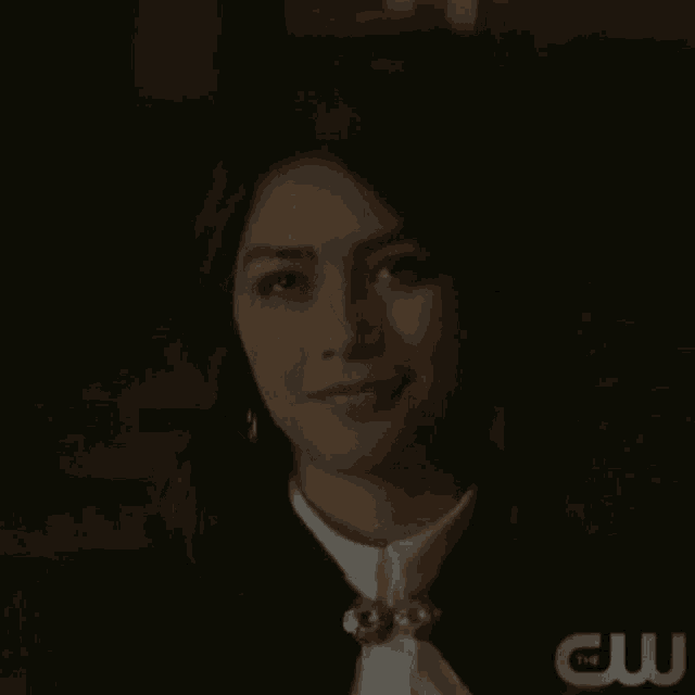 a woman is smiling in a dark room while wearing a black jacket and white shirt .