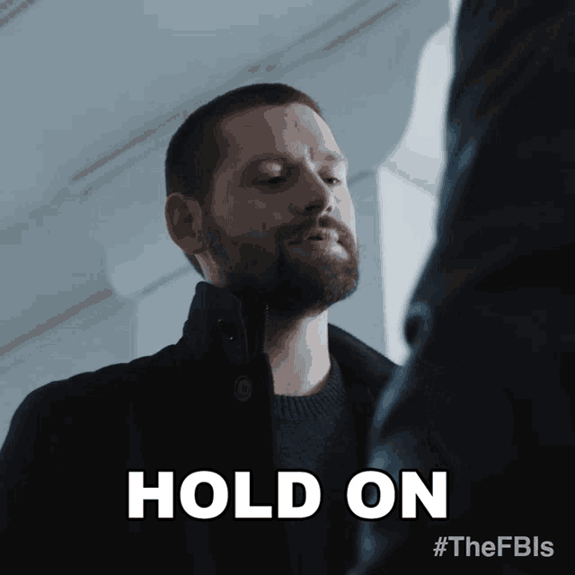 a man with a beard is holding another man 's hand and says hold on
