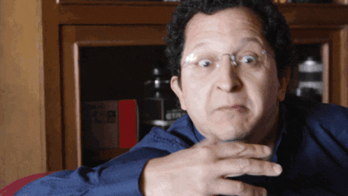 a man wearing glasses and a blue shirt is making a surprised face