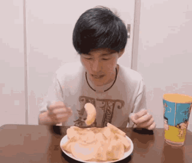 a young man is sitting at a table eating potato chips with a fork .