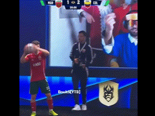 a man in a red shirt is holding a soccer ball in front of a screen with a score of 1 to 2 .