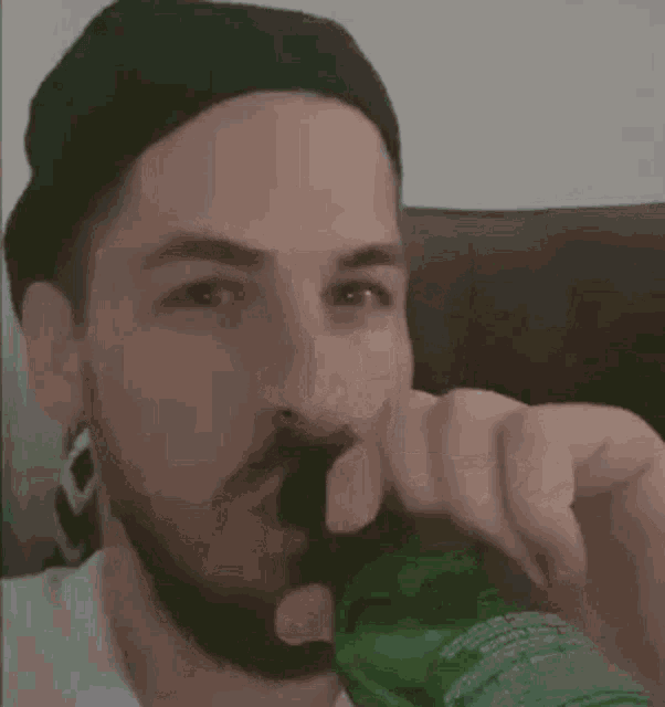a man with a beard is drinking from a green bottle with his finger .