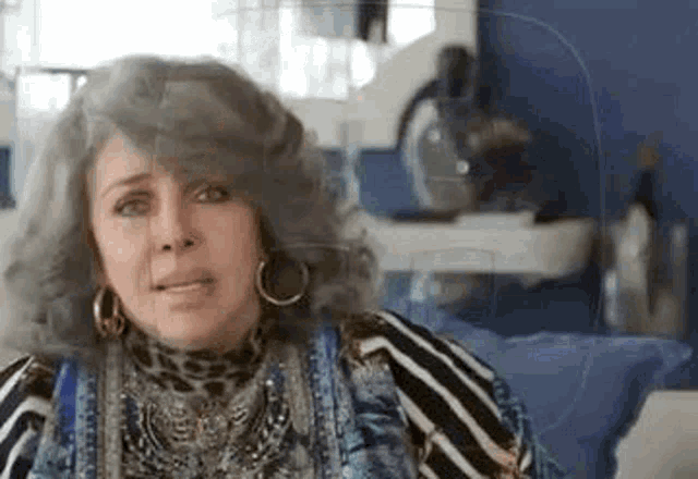 a woman with gray hair and hoop earrings is sitting on a couch in a room .