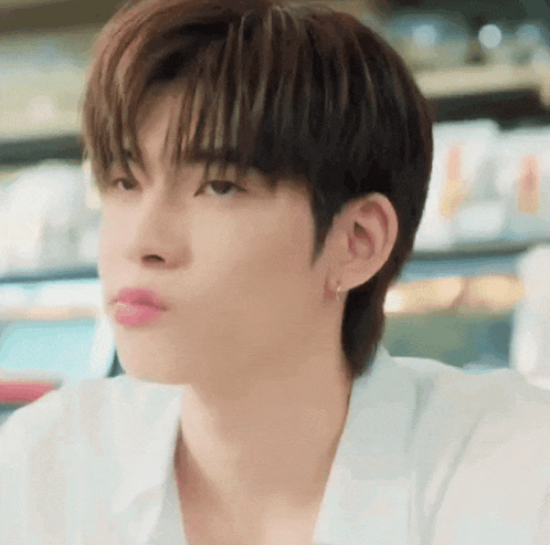 a close up of a young man 's face with a white shirt and earrings .