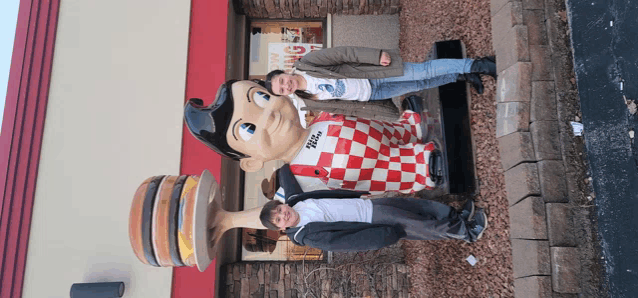 a boy and a girl pose in front of a statue of big boy