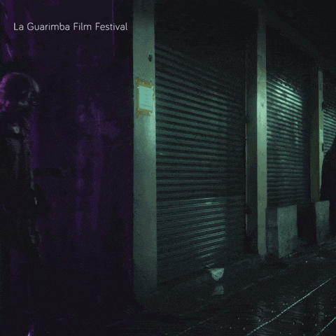 a woman walking down a dark street with the words la guarimba film festival written above her
