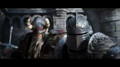 a man with a beard and horns is standing next to a man in armor holding a sword .
