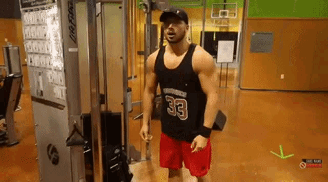 a man wearing a black tank top with the number 33 on it is standing in a gym