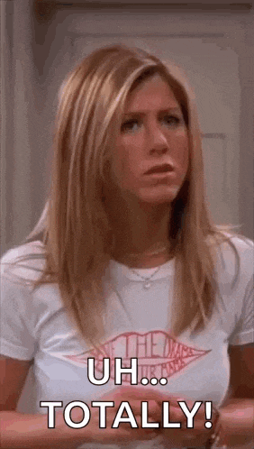 a woman in a white t-shirt is standing in front of a door and saying `` uh ... totally ! ''
