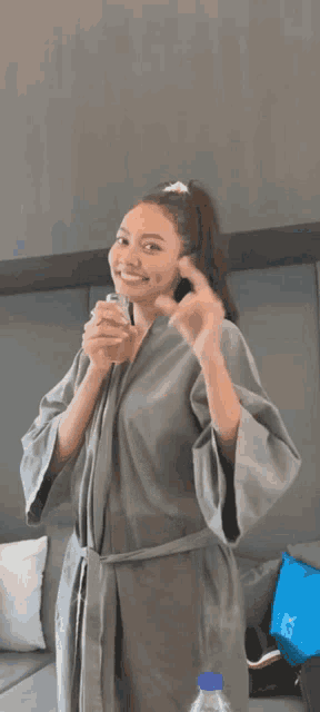 a woman in a robe is holding a glass of water and giving the middle finger