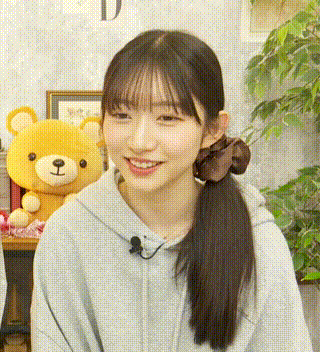 a close up of a woman wearing a ponytail and a hoodie with a teddy bear in the background .