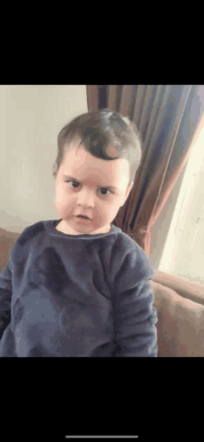a little boy in a blue shirt is sitting on a couch