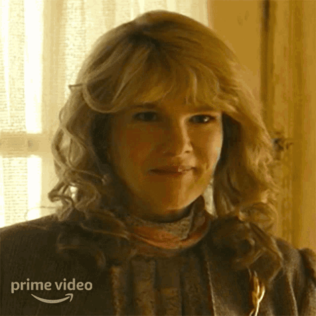 a woman with blonde hair is smiling in front of a window with the words prime video on the bottom