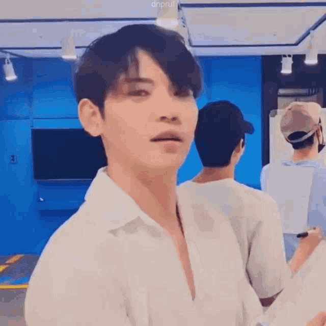 a man in a white shirt is standing in front of a blue wall and looking at the camera .